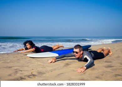 man instructor demonstrating how to stand up on surfboard to indian woman in surf class in Goa sea