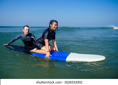man instructor demonstrating how to stand up on surfboard to indian woman in surf class in Goa sea