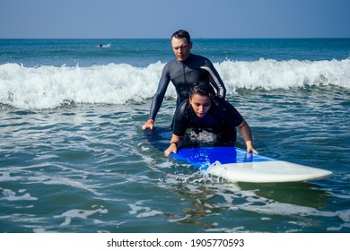 man instructor demonstrating how to stand up on surfboard to indian woman in surf class in Goa sea