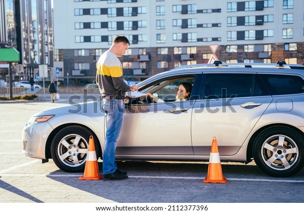 Man instructor standing\
outside of car and teaching his female student how parking car\
correctly.
