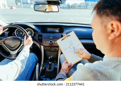 Man instructor teaching student about traffic rules on first automobile driving class. Examiner sitting with her student inside a car. Writing points. Driving instructor writing points
