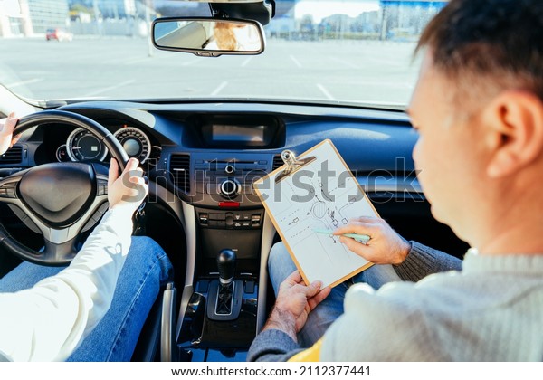 Man\
instructor teaching student about traffic rules on first automobile\
driving class. Examiner sitting with her student inside a car.\
Writing points. Driving instructor writing\
points