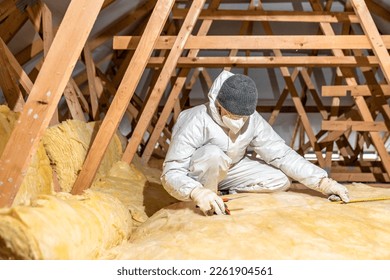 man insulates the roof and ceiling of the house with glass wool - Shutterstock ID 2261904561