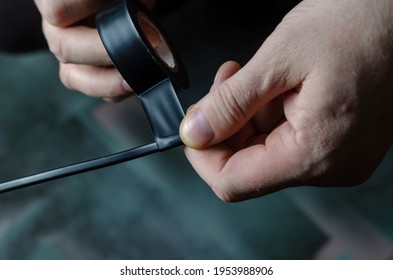 A man is insulating a black electrical wire. Close-up of male hands holding a roll of black duct tape for electrical work. Adult male, Caucasian. Inside the room. Selective focus. - Shutterstock ID 1953988906