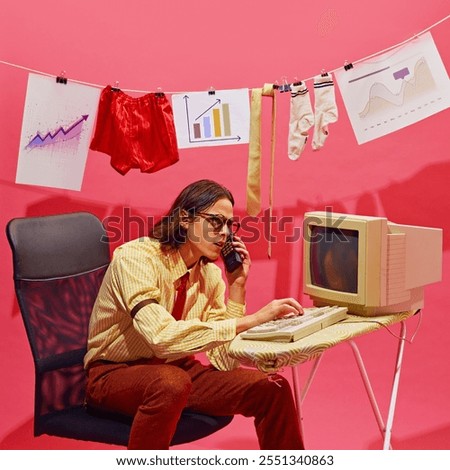 Man intently looks at document while typing on vintage computer. There are graphs and charts hanging from line along with socks and red shorts. Concept of business, work-life balance. Nostalgia.