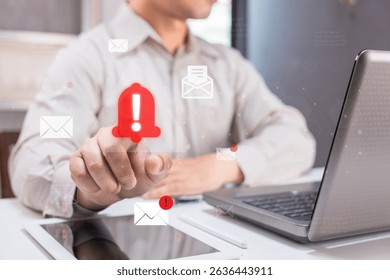A man interacts with a digital notification alert on a transparent screen, with laptops and tablets in a modern office setting.