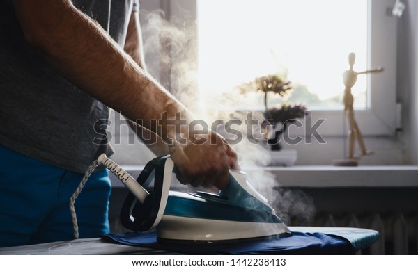 Man is ironing clothes. The concept of caring\
for the home, helping men in household chores. The man uses an iron\
to iron the child\'s\
clothes.