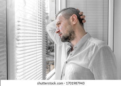 Man in isolation looking through window blinds. Coronavirus outbreak. Man looks at a sunny street through the window blinds