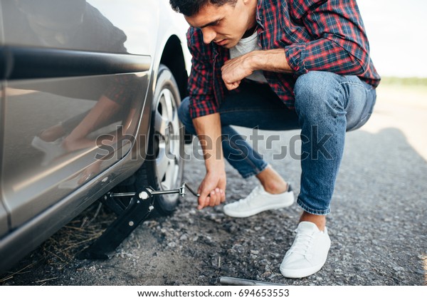 Man jack up broken\
car, wheel replacement