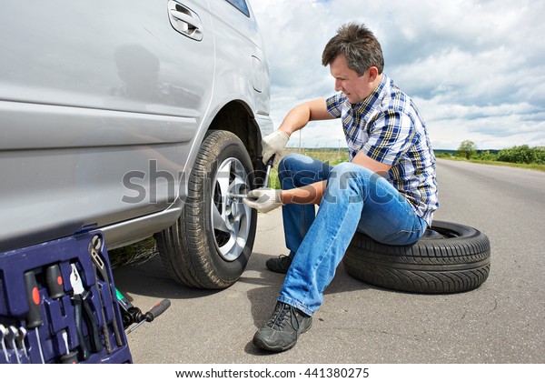 Man with\
jack changing a spare tire of car on\
road