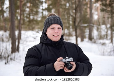 Man in a jacket and a hat with retro camera in winter forest.