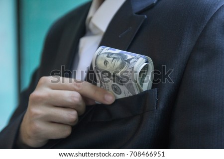 A man in a jacket or a tuxedo puts a bundle of hundred-dollar bills in his breast pocket, close up