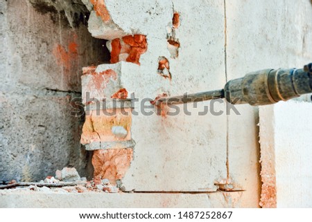 A man with a jackhammer makes an opening in the wall.