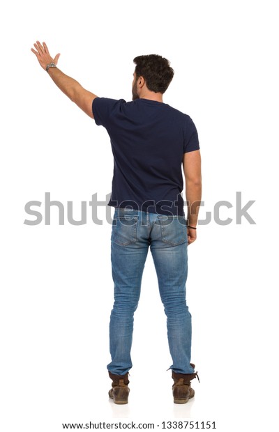 ジーンズと青のtシャツを着た男性が腕を上げ 左手を振って立っている 背面図 白い背景に全長のスタジオショット の写真素材 今すぐ編集
