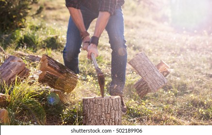 Man In Jeans And Checkered Shirt Chopping Wood With Axe