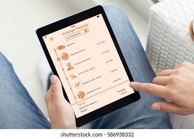 man in jeans on sofa holding tablet computer with app tracking delivery package