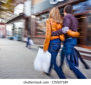 Man in jeans and a woman in a leather jacket walking down the street hugging. Intentional motion blur