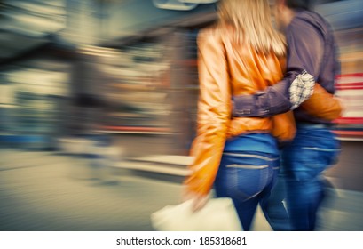 Man in jeans and a woman in a leather jacket walking down the street hugging. Intentional motion blur and color shift