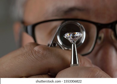 Man jeweller examines polished diamond through magnifier. Buyer checking diamond. Diamond jewellery under grading. Jeweller looking through loupe.