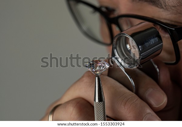 Man jeweller examines polished diamond through magnifier. Buyer checking diamond. Cut and polished diamond. Diamond jewellery under grading. Jeweller looking through loupe.