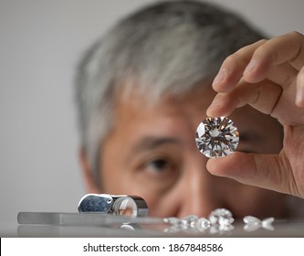 Man jeweller looking at diamond. Holding in hand. Close up brilliant. Gem grading at workshop. Cut and polished diamonds.
