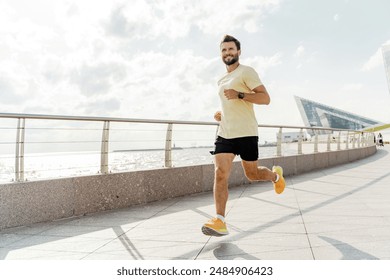 A man jogging on a waterfront promenade on a sunny day, wearing a yellow shirt and black shorts, with modern buildings in the background. - Powered by Shutterstock