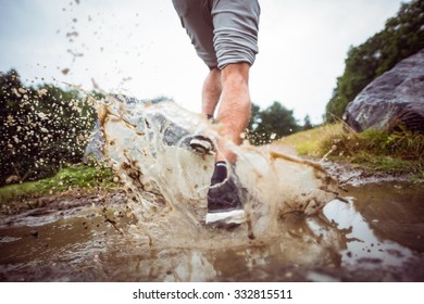 Man Jogging Through Muddy Puddles In The Countryside