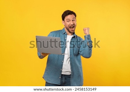 A man is joyfully celebrating while holding a laptop in his hands. He is likely reacting to good news or completing a successful task on the device.