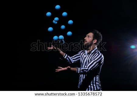 Man juggling blue balls on black background. Stylish Man with black and white shirt posing for the camera.