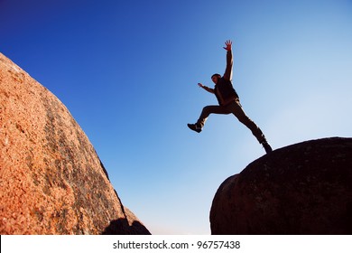 man jumping cliff with blue sky