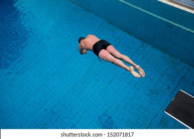 Man Jumping From Diving Board At Public Swimming Pool