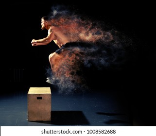 Man jumping on fit box in gym. Male with naked torso exercises jump on the dark background. 