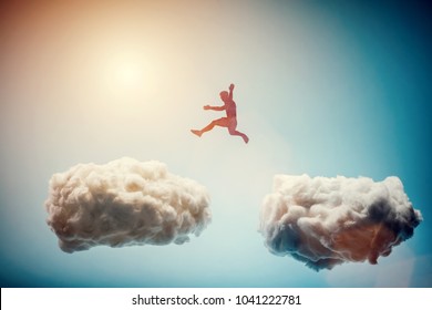 Man jumping from one cloud to another. Taking risks and challenge concept. Overcoming problems, winning. - Shutterstock ID 1041222781