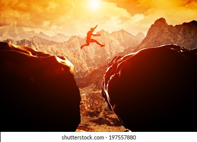 Man jumping over precipice between two rocky mountains at sunset. Freedom, risk, challenge, success. - Shutterstock ID 197557880