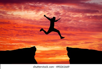 Man jumping over rocks with gap on sunset fiery background. Element of design.  