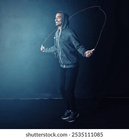 Man, jumping rope and fitness with smile from cardio and impact training for boxing in gym studio. Exercise, African athlete and health with wellness, workout and skip for sport and dark background - Powered by Shutterstock