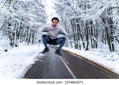 Man jumping for a warm up before he goes on a run in the winter on a mountain road - Shutterstock ID 2254862071