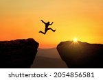 Man jumps from cliff to cliff over a precipice at sunset, a creative idea. Success and Risk Concept