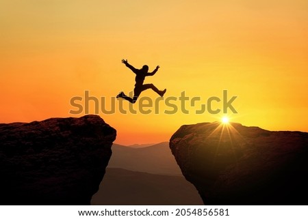 Man jumps from cliff to cliff over a precipice at sunset, a creative idea. Success and Risk Concept