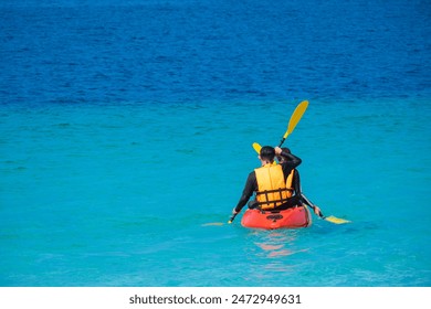 Man kayaking in the blue sea and clear water. You can see corals under the sea. - Powered by Shutterstock