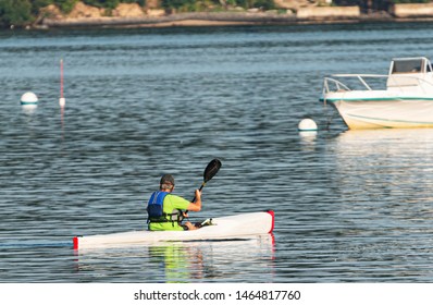 A Man Is Kayaking In A Harbor On The North Shore Of Long Island Paddling Around Moored Boats.