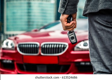 Man with key fob  standing near red luxury car 