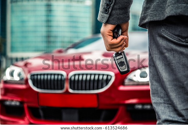 Man with key\
fob  standing near red luxury car\
