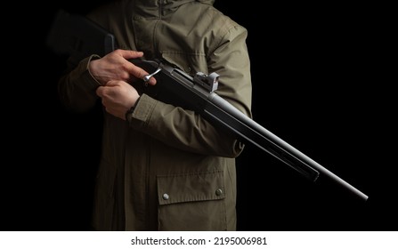 A Man In A Khaki Jacket Holds A Bolt Rifle With A Reflex Sight In His Hands. Hunter With Weapons. Dark Background.