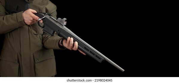 A Man In A Khaki Jacket Holds A Bolt Rifle With A Reflex Sight In His Hands. Hunter With Weapons. Dark Background.