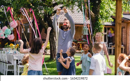 Man With Kids On Birthday Party Playing Outdoors In Garden In Summer.