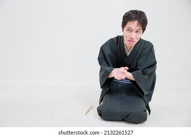 A man in a kimono begs while rubbing his hands