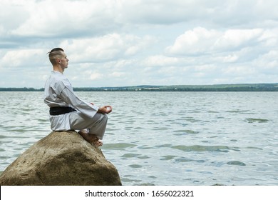 A man in a kimono sits on a rock, under it is the sea.  Master with a black belt.  Practical class in karate.  The technique of meditation.  Cleansing and thinking about life before the fight.  - Powered by Shutterstock