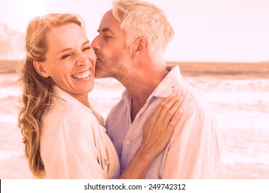 Man kissing his smiling partner on the cheek at the beach on a sunny day