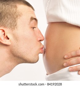 Man kissing his wife's belly at home against wall
